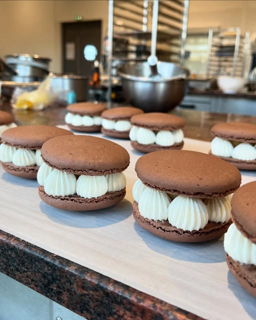 À l’atelier, des macarons garnis de crème sont disposés sur le plan de travail